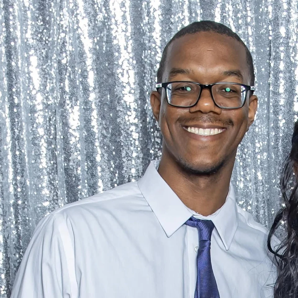 Brian Cole Jr. smiling, wearing glasses, a light blue shirt and a tie